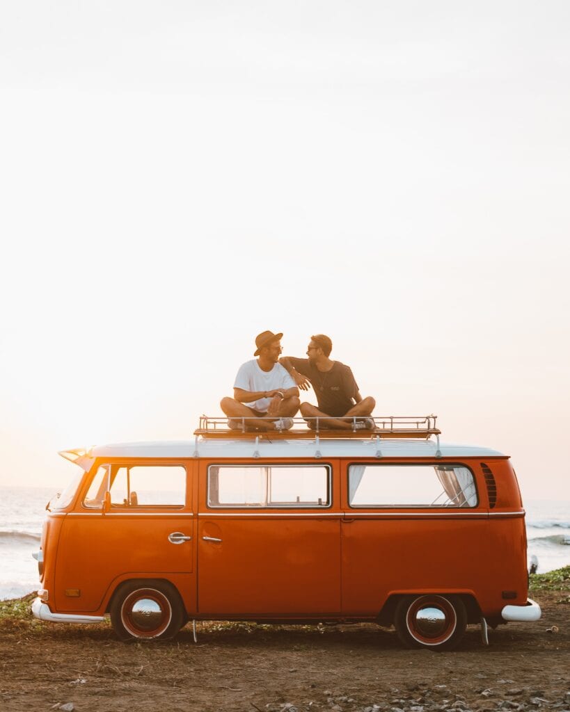 two men sat on top of a red campervan