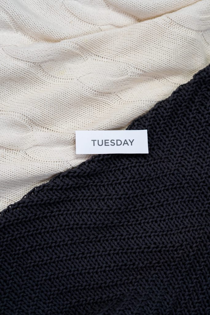 a note with the word Tuesday in bold letters laid on some black and white material